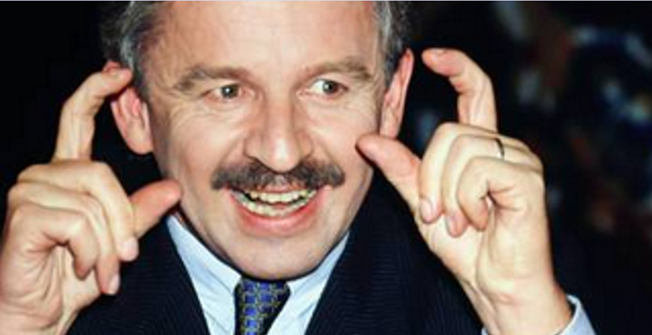 A person with a mustache pointing his fingers

Description automatically generated